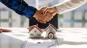 An image of two people shaking hands with two small house models in the background.